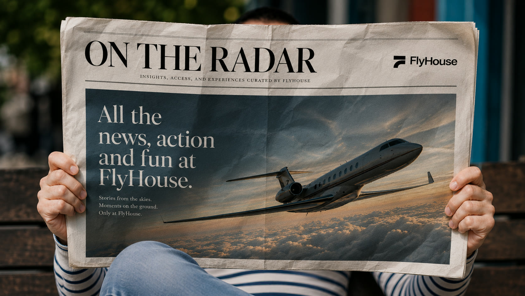 A reader holds the FlyHouse 'On the Radar' newspaper, a jet in flight on the spread, the FlyHouse logo at the masthead